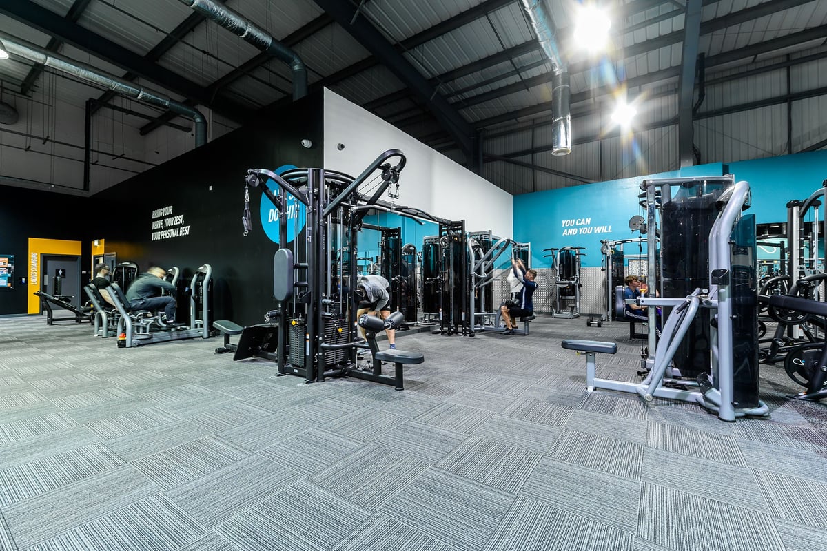 PureGym Bromborough: Functional training area with squat racks, cable machines, free weights, and rubberized flooring.
