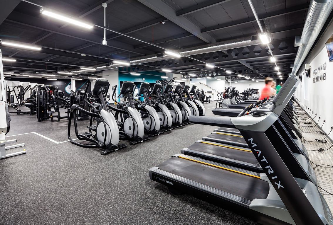 PureGym Manchester Stretford: Rows of treadmills, ellipticals, and exercise bikes in a brightly lit gym interior.