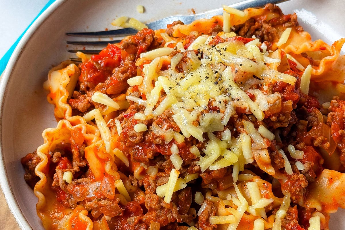 Pasta with meat sauce topped with grated cheese and black pepper on a beige plate.