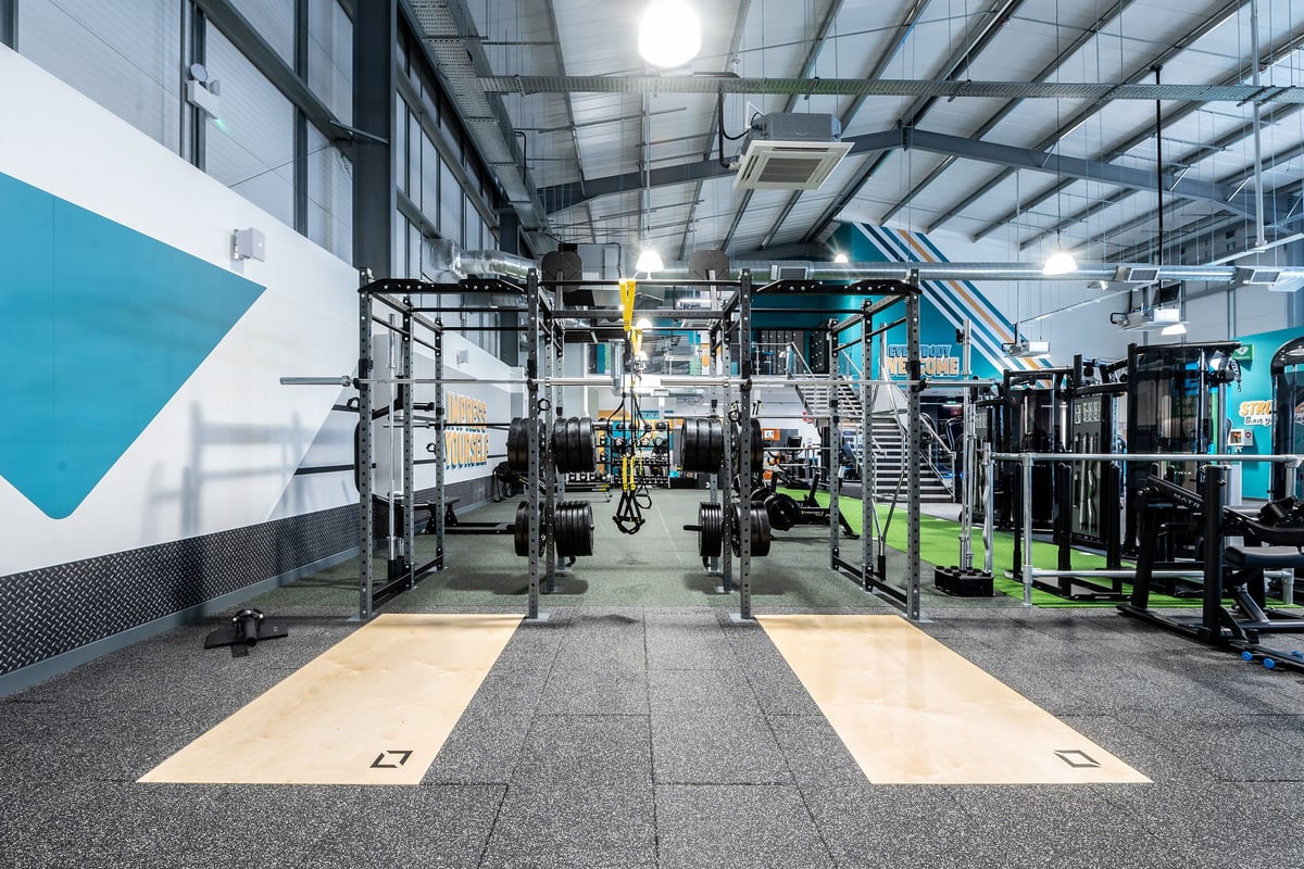 PureGym Cirencester: Strength training rig, squat racks, free weights, rubberized flooring in a modern gym interior.