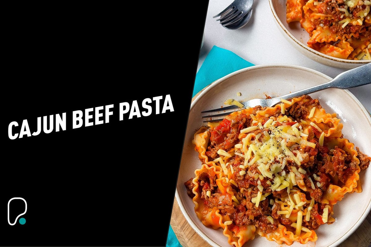 Two plates of Cajun beef pasta topped with grated cheese and black pepper with forks