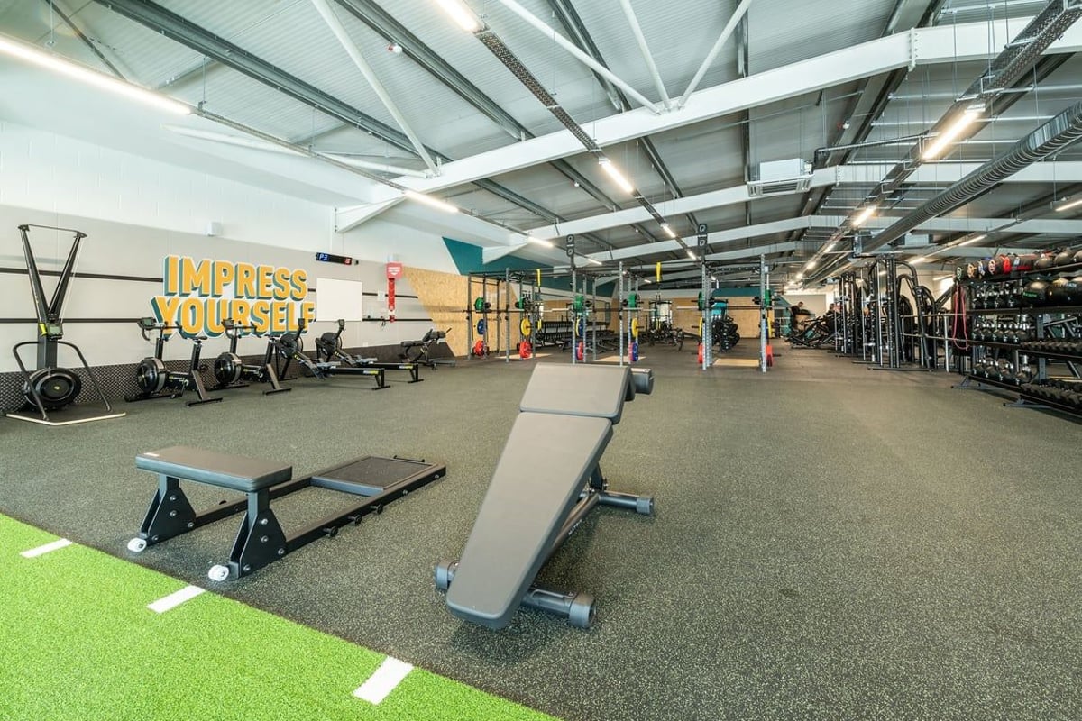 PureGym London Colney: Gym with weight racks, benches, rubberized flooring, motivational mural "Express Yourself" on wall.