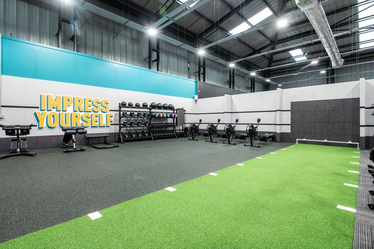 PureGym Dunfermline: Rows of cardio machines, free weights stands, green turf area, and mirrored walls.