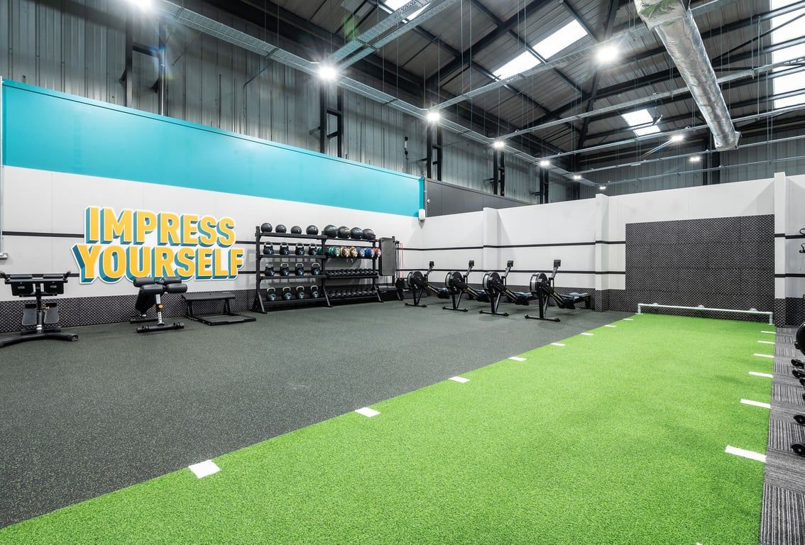 PureGym Dunfermline: Rows of cardio machines, free weights stands, green turf area, and mirrored walls.