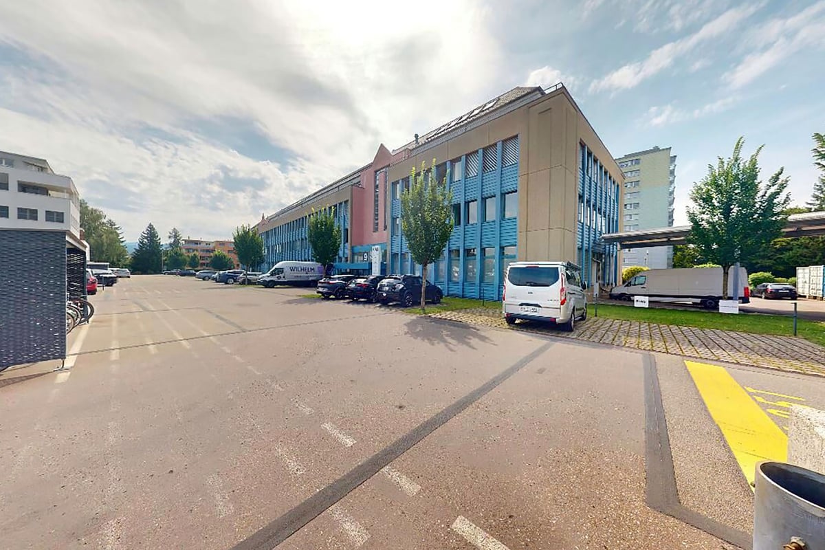 PureGym Wetzikon: Aussenansicht des Bürogebäudes mit geparkten Autos entlang der Strasse und dem Bürgersteig, der zum Eingang führt.