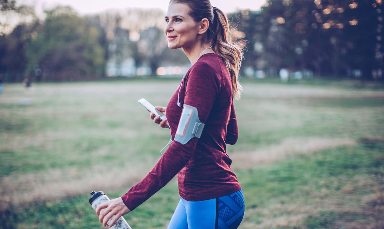 Woman in sportswear holding a water bottle and phone in a park at dusk