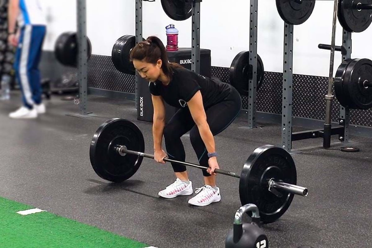 Woman lifting barbell in gym with kettlebell and weights in background