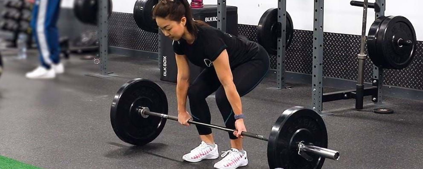 Woman lifting barbell in gym with kettlebell and weights in background