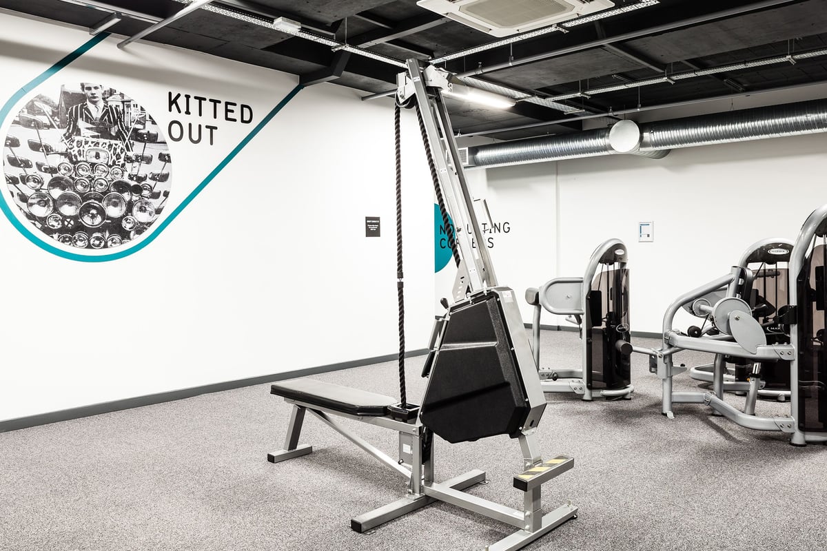 PureGym Altrincham: Lat pulldown machine, weight benches, cable crossover station, rubberized flooring, exposed ceiling.