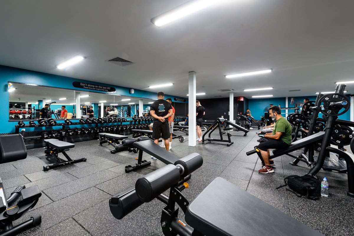 PureGym London Hayes: Rows of weight benches, free weights, resistance machines, and rubberized flooring in a modern gym.