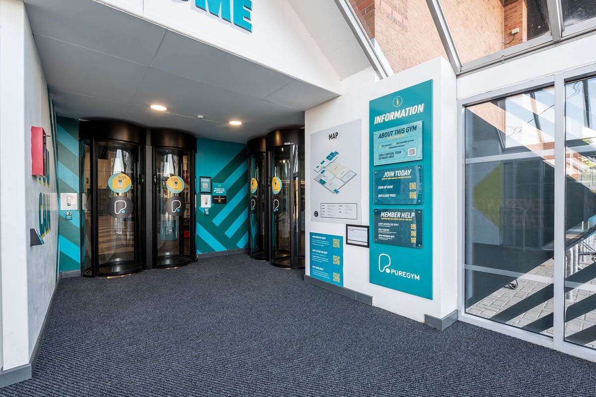PureGym York: Gym entrance with revolving doors, information board displaying membership details.