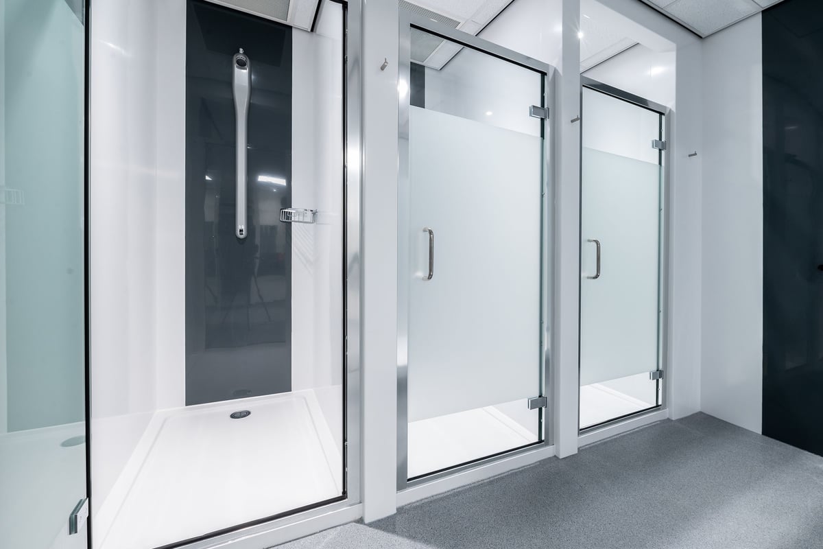 PureGym Maidstone The Mall: Glass shower stalls, tile floors, metallic accents - appears to be changing rooms.
