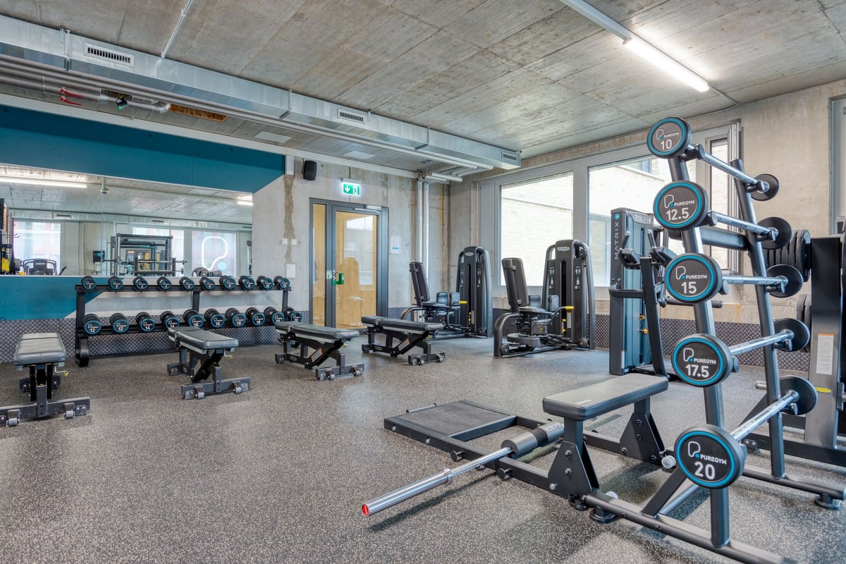PureGym Lenzburg : espace fitness avec appareils de musculation, bancs, haltères et murs en miroir.