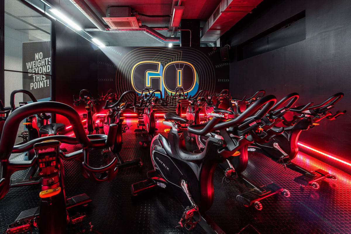 PureGym London Greenwich: Rows of spin bikes with red neon lighting, motivational signage, and mirrored walls.