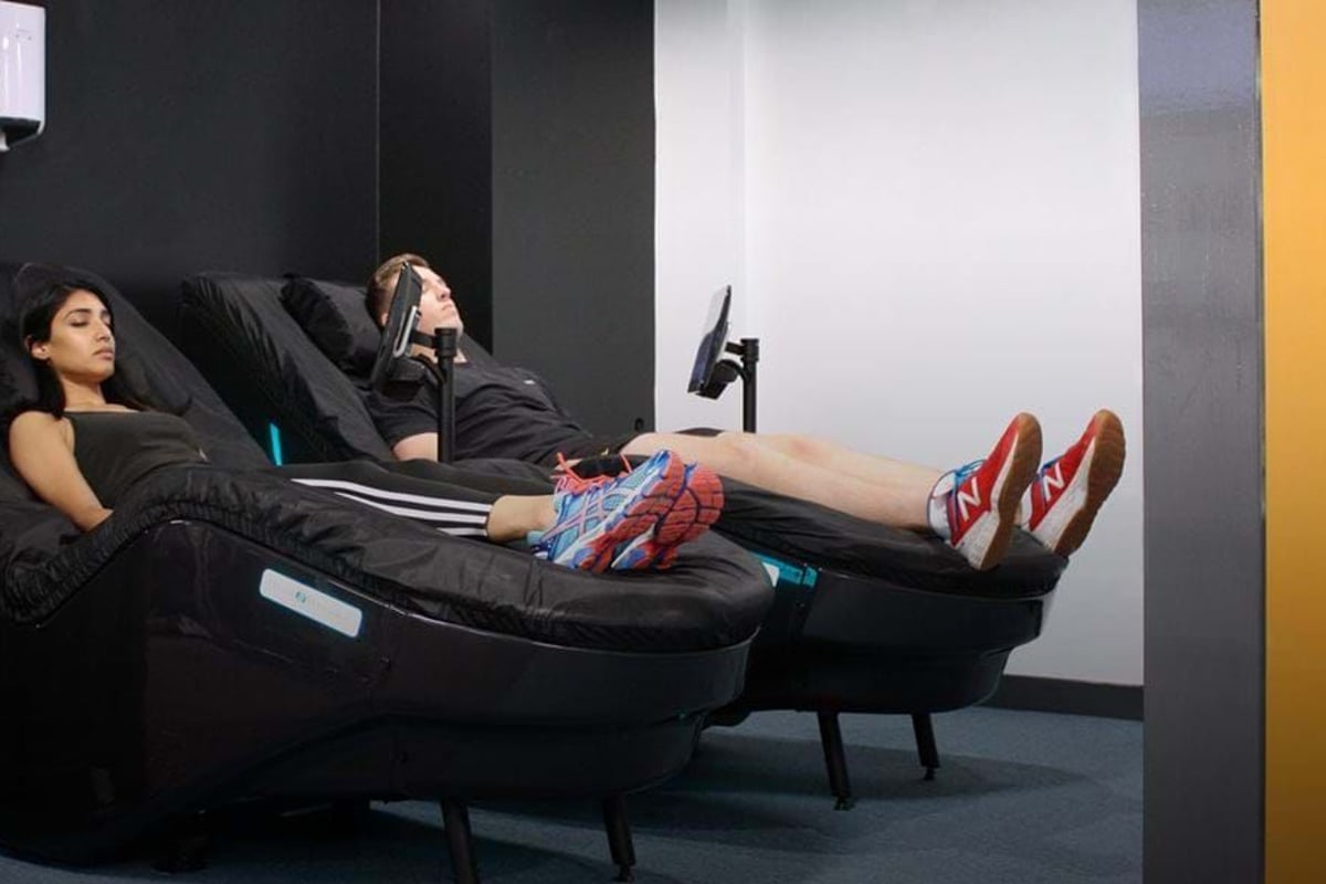 Two people reclining on black massage chairs in a room with black and white walls