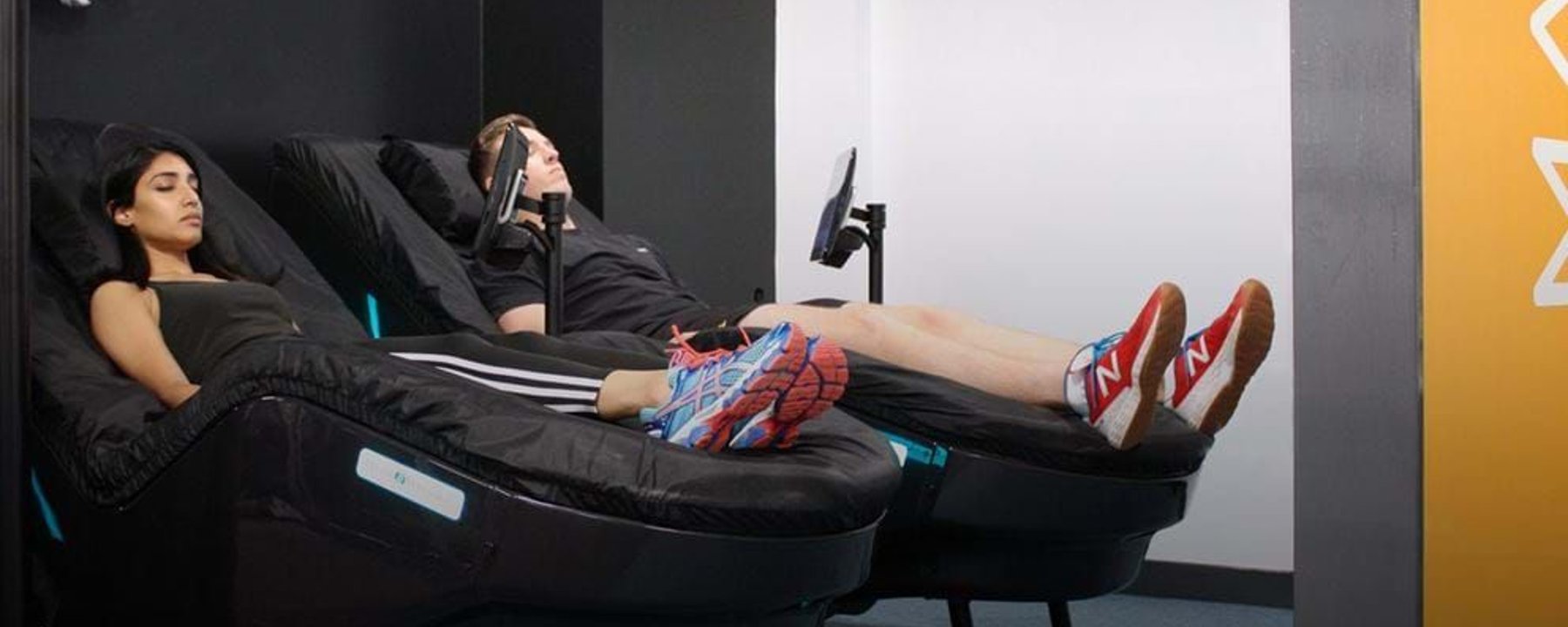 Two people reclining on black massage chairs in a room with black and white walls
