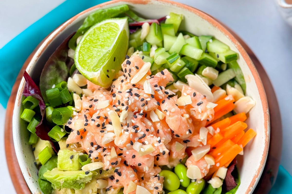 Bowl of poke with diced salmon, avocado, edamame, cucumber, carrot, lime, and sesame seeds