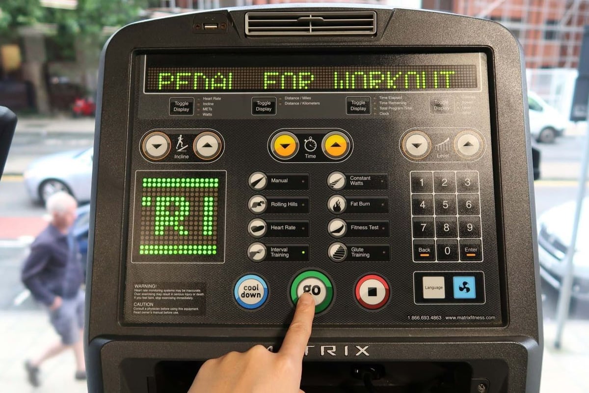 Finger pressing green go button on treadmill control panel with street view behind