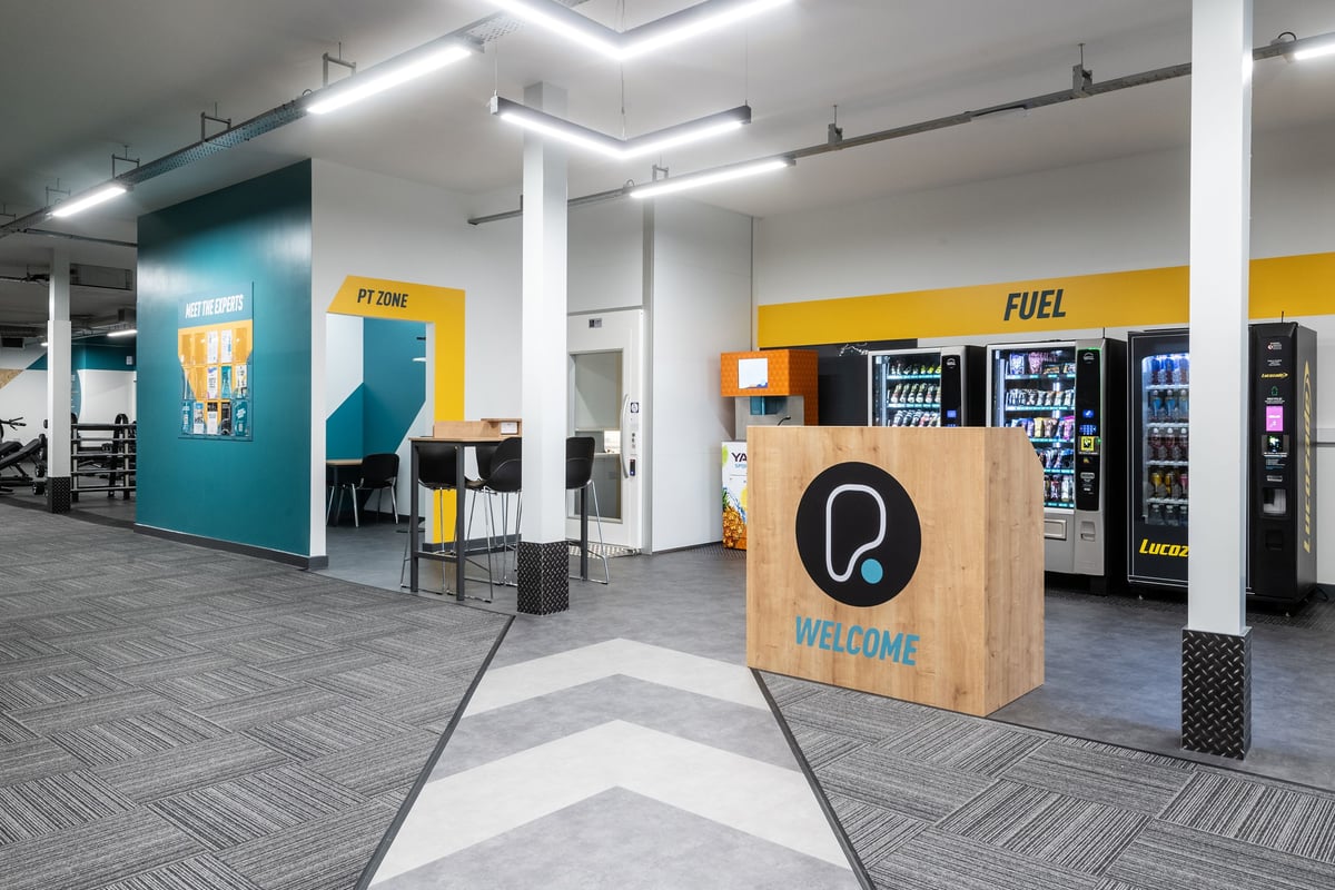 PureGym Derby Kingsway Retail Park: Welcome area with tables and chairs, vending machines, and personal training zone.