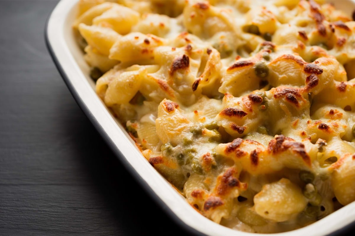 Baked pasta shells with melted cheese and green peas in a white dish on black surface