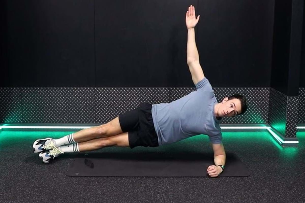 Man in sportswear doing side plank exercise on a mat in a gym room with green lights