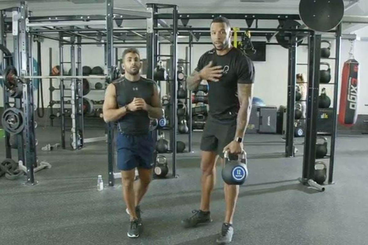 Two men in gym gear standing in a gym with kettlebells and weights around them