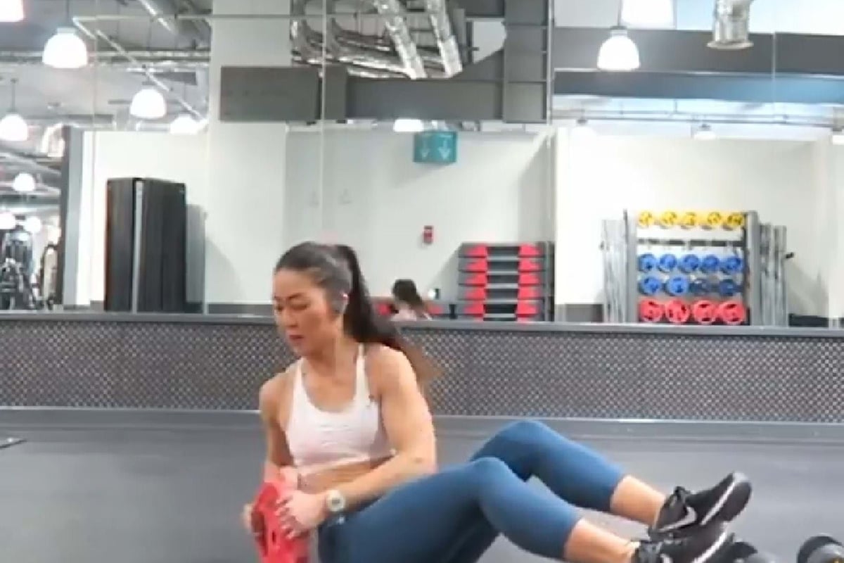 Woman in sportswear doing Russian twists with a red weight plate in a gym