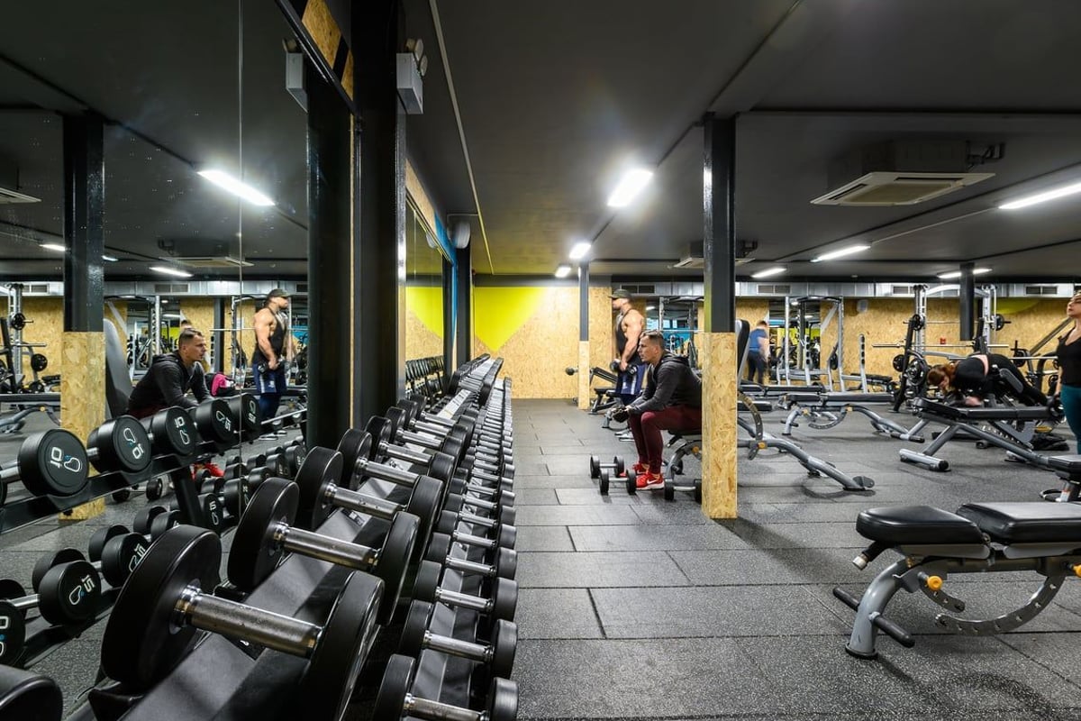 PureGym Reading Caversham Road: Rows of dumbbell racks, weight benches, and exercise equipment in a dimly lit gym setting.