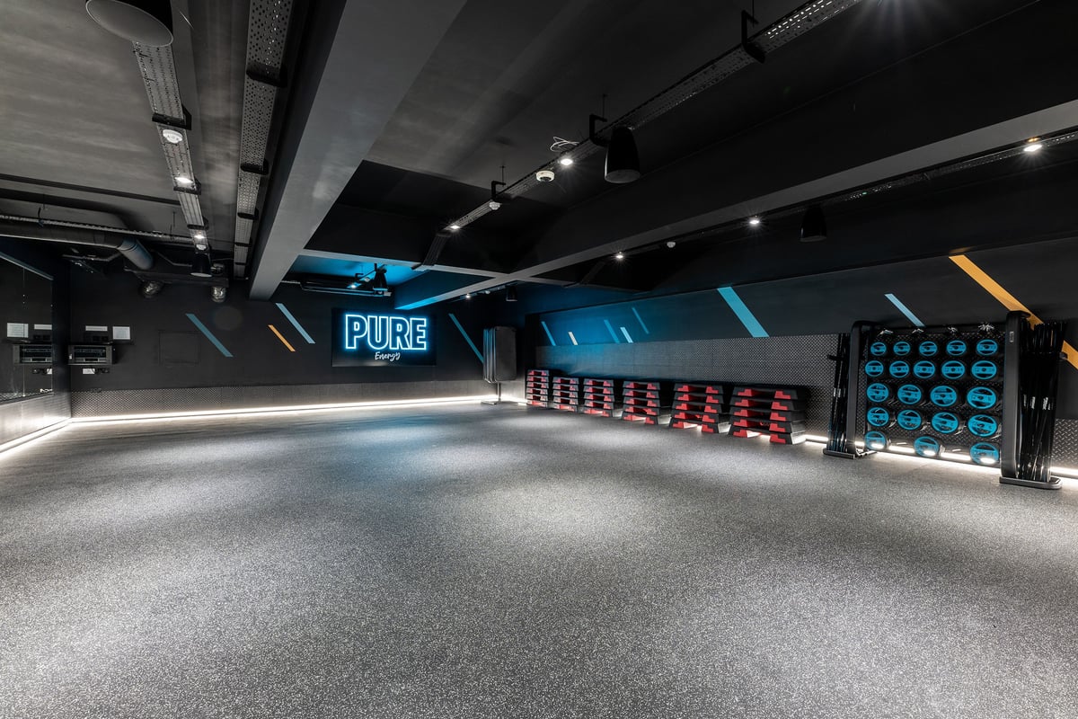 PureGym Manchester First Street: Pure fitness studio with weight racks, vibrant neon lighting, and rubberized flooring.