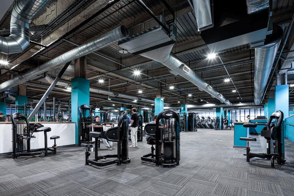 PureGym Cardiff Central: Weight machines, benches, mirrors, ventilation pipes overhead in a gym setting.