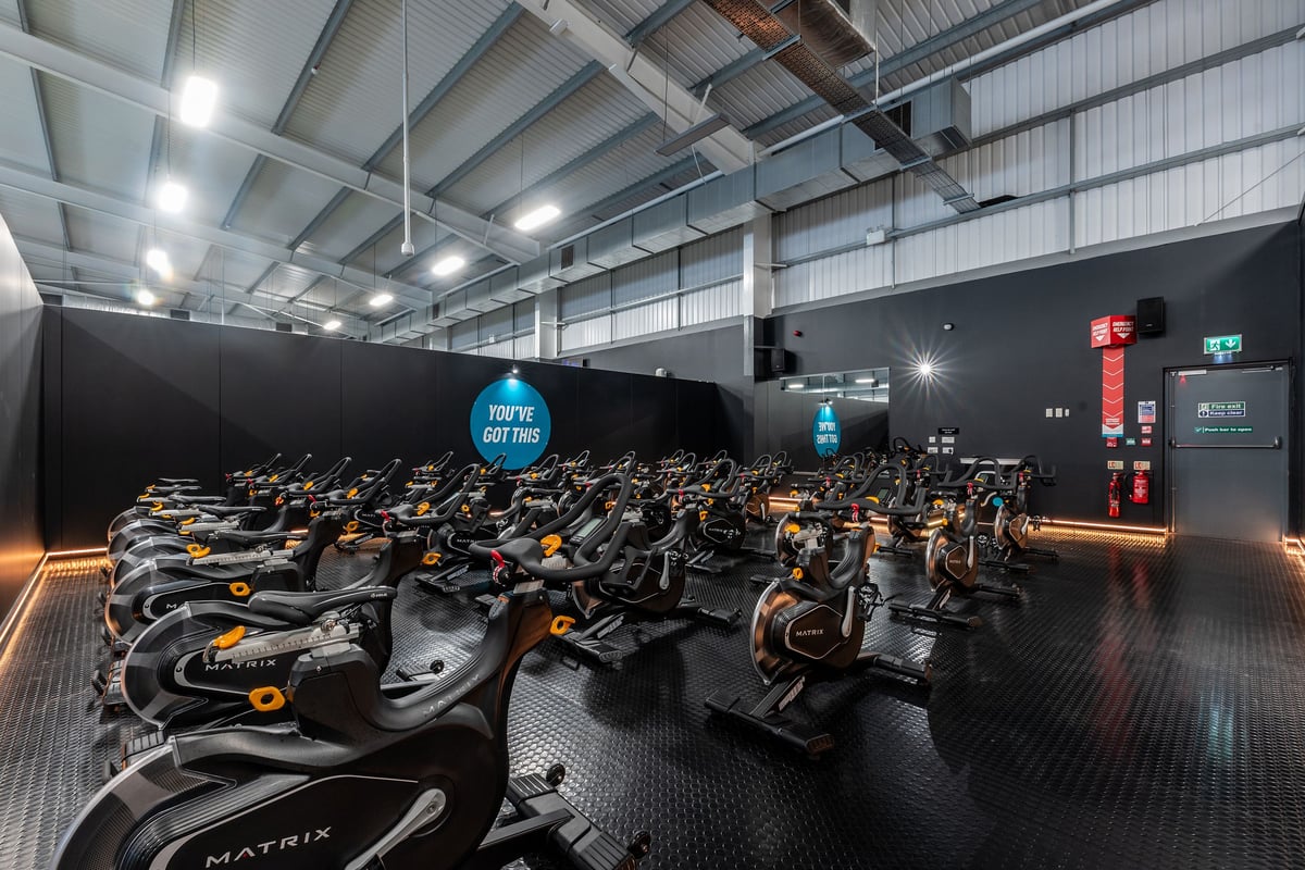 PureGym Widnes: Rows of stationary bikes in a dimly lit indoor cycling studio.
