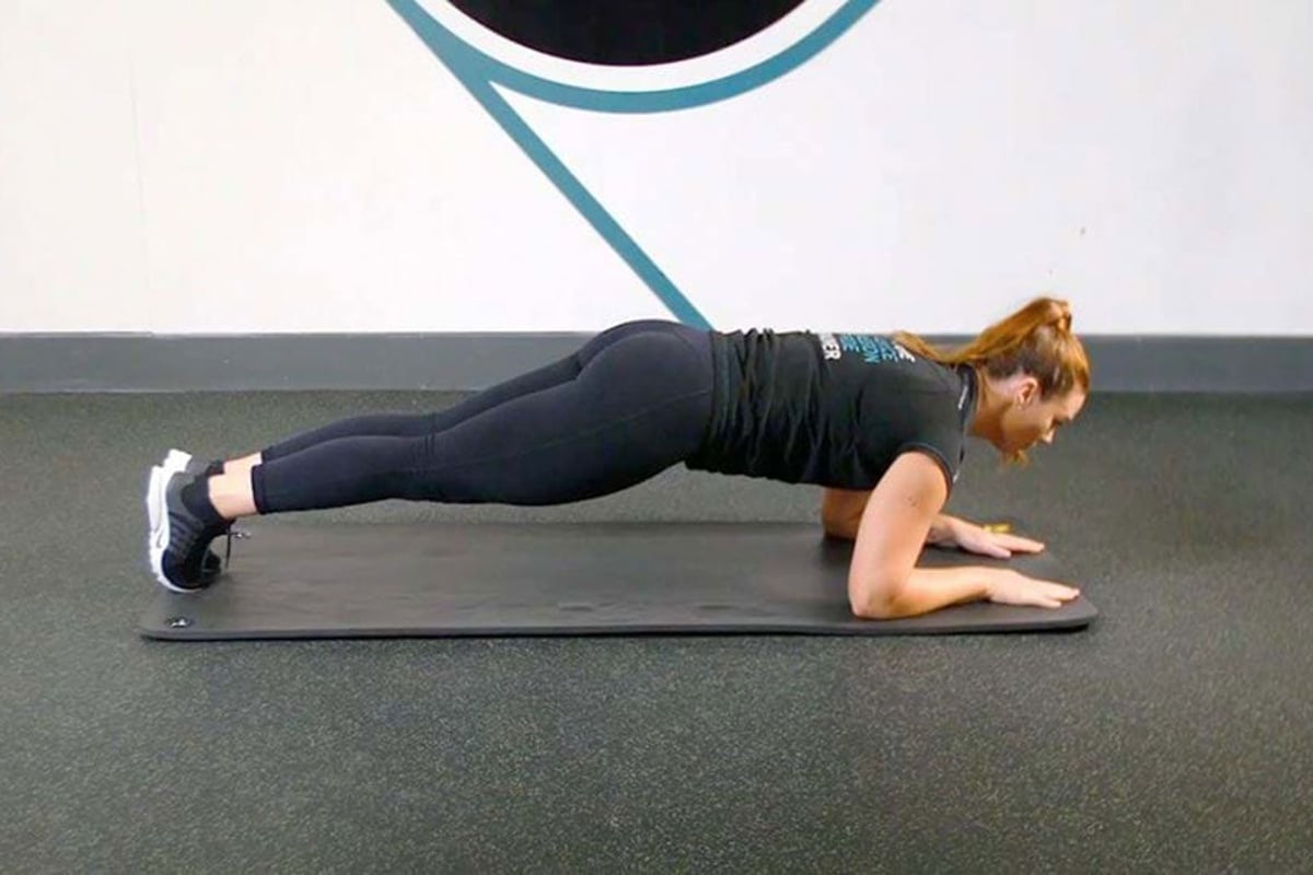 Frau macht eine Plankenübung auf einer Matte in einem Fitnessstudio mit blauen Wandgrafike
