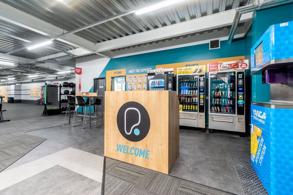 PureGym Banbury Cross Retail Park: Vending machines, seating area, and welcoming reception counter inside facility.
