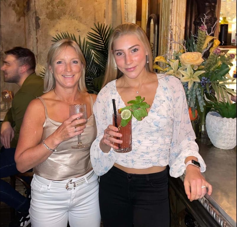 Two women holding drinks with floral decorations behind them