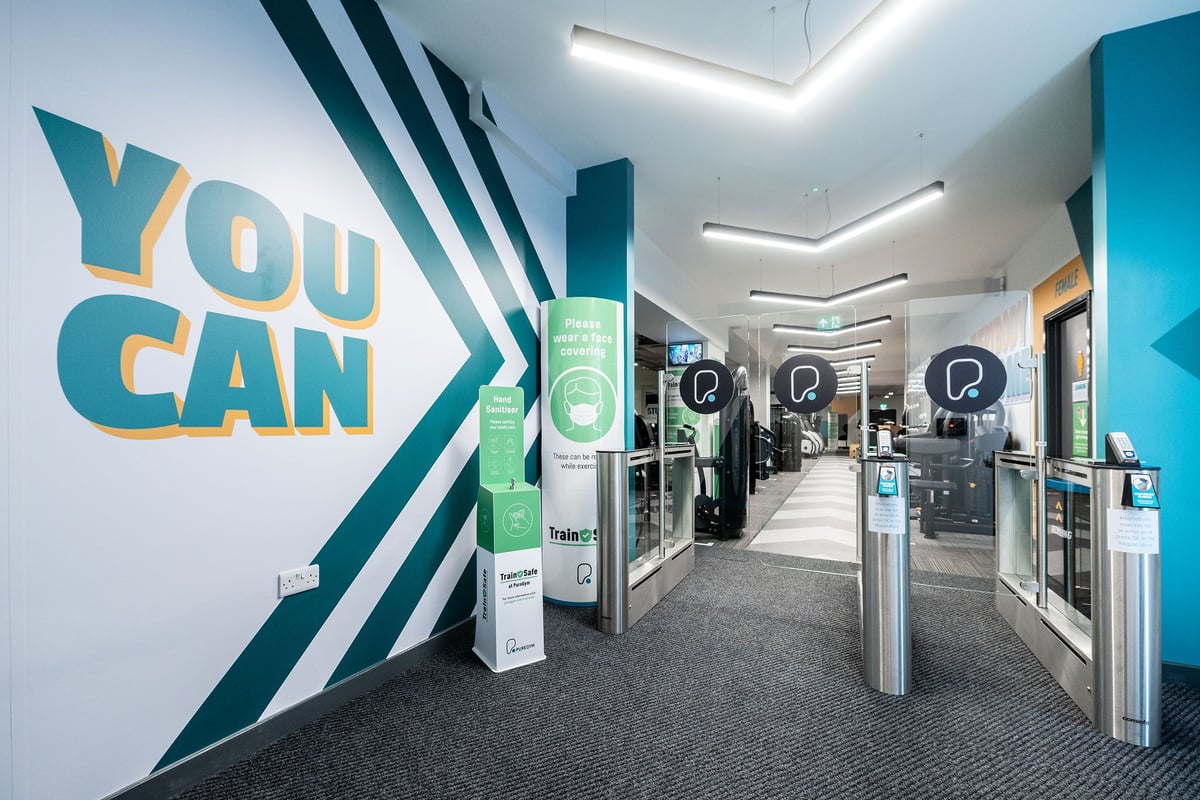 PureGym London Twickenham: Access turnstiles, self-service kiosks, motivational wall graphics in facility interior.