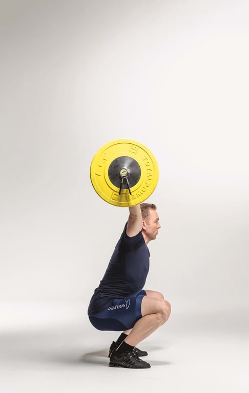 Man in navy sportswear squatting while holding a barbell with yellow weights overhead