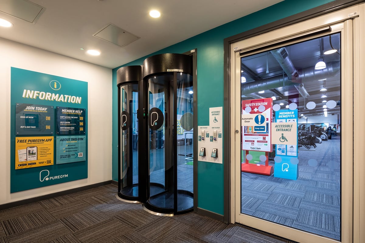 PureGym Cardiff Gate: Information desk area with revolving door entry and posted signage.