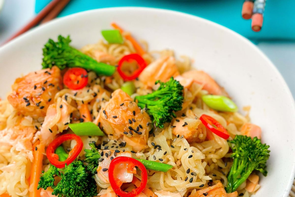 Noodles with salmon, broccoli, carrot strips, red chili slices, and black sesame seeds in