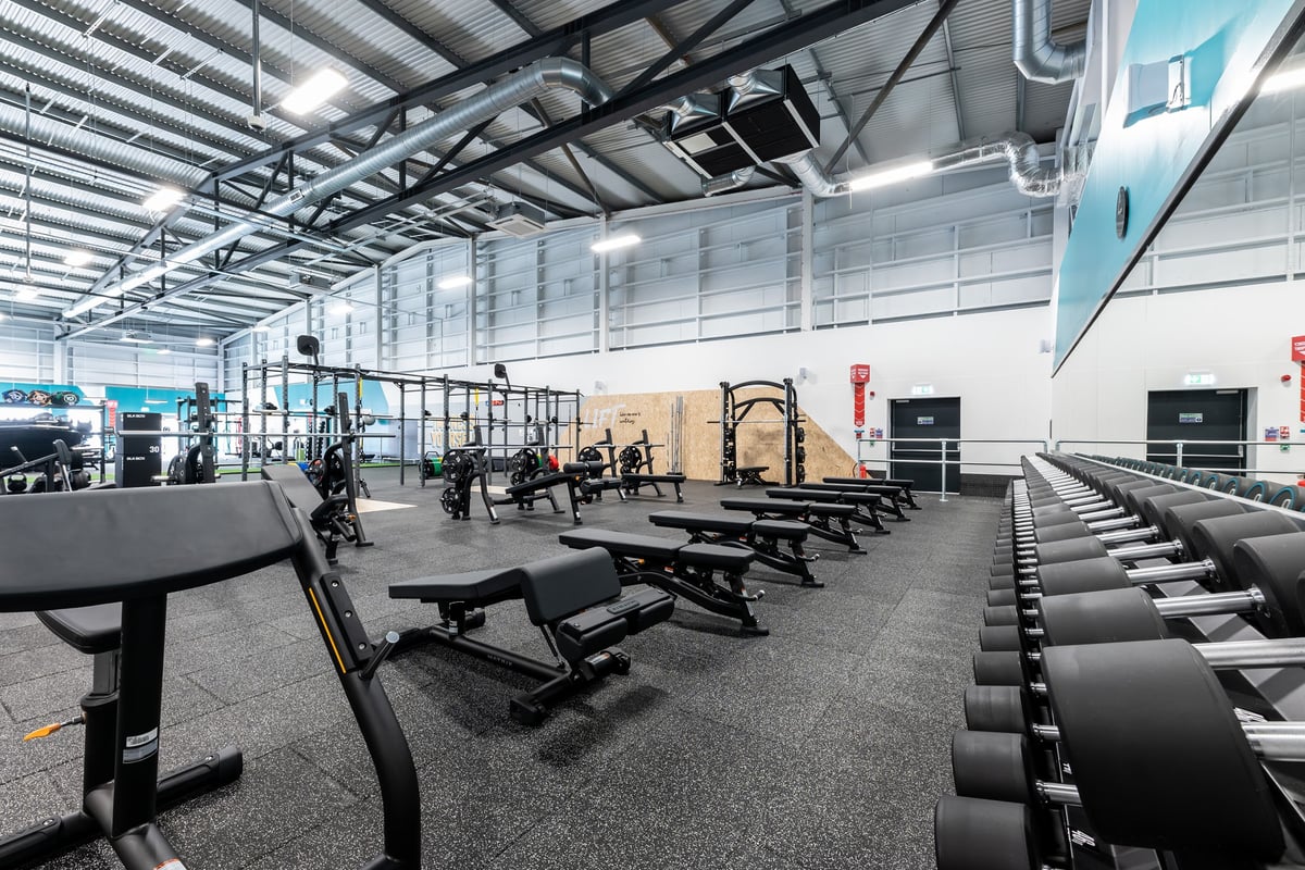 PureGym Ipswich Ravenswood: Rows of benches, racks for free weights, and rubberized gym flooring.