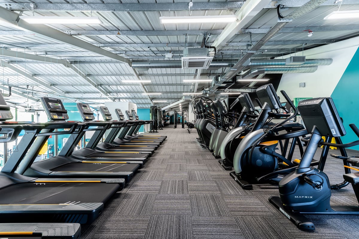PureGym Bath Victoria Park: Rows of treadmills and exercise bikes in a well-lit gym interior with exposed ceilings.