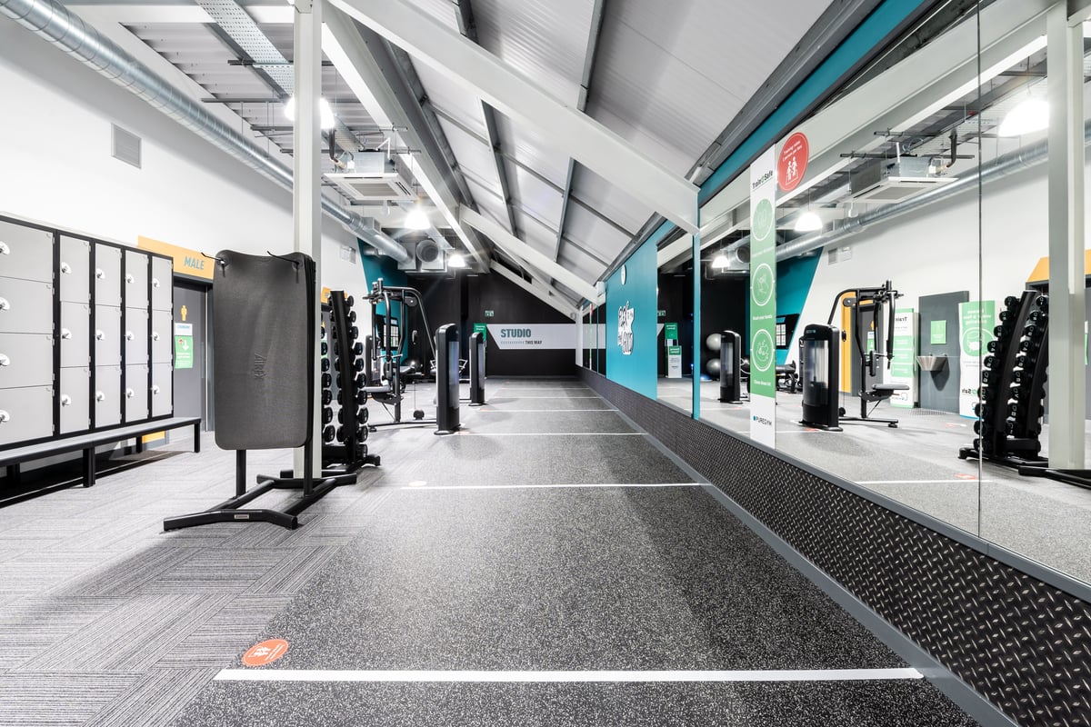 PureGym Plymouth Marsh Mills: Gym interior with weight machines, free weights, rubberized flooring, and mirrors along walls.