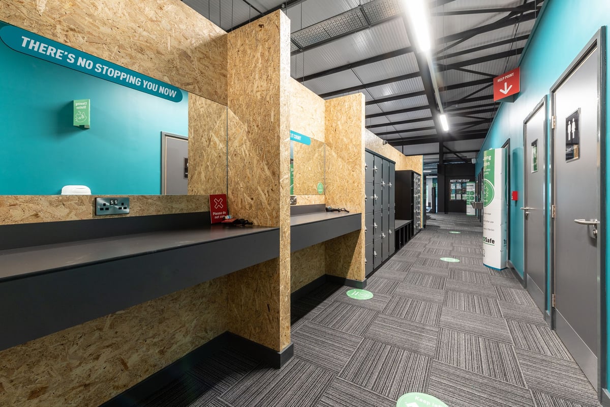 PureGym Kirkcaldy: Hallway with seating, lockers, and teal accent walls promoting fitness motivation.