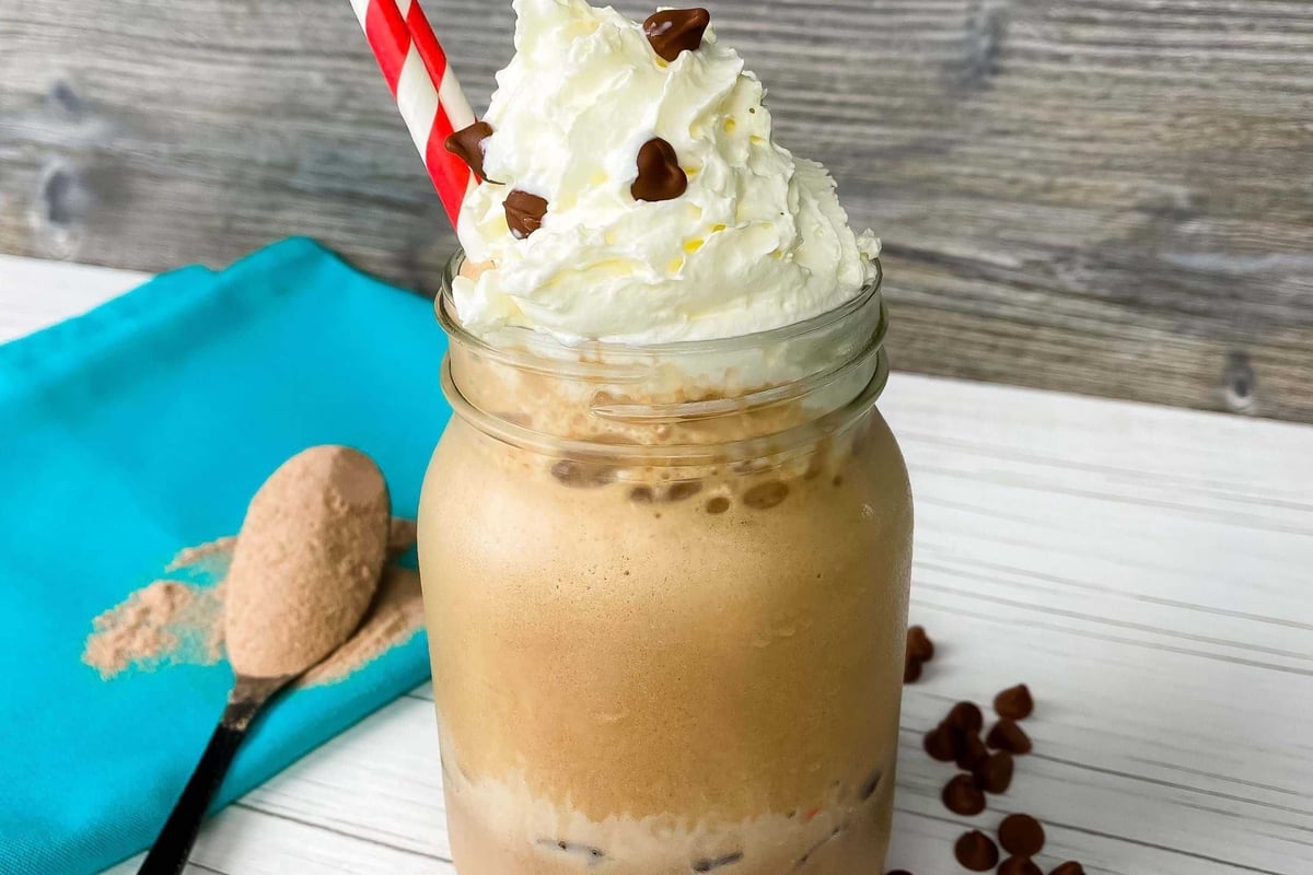 Iced coffee with whipped cream and chocolate chips in a jar with a red striped straw