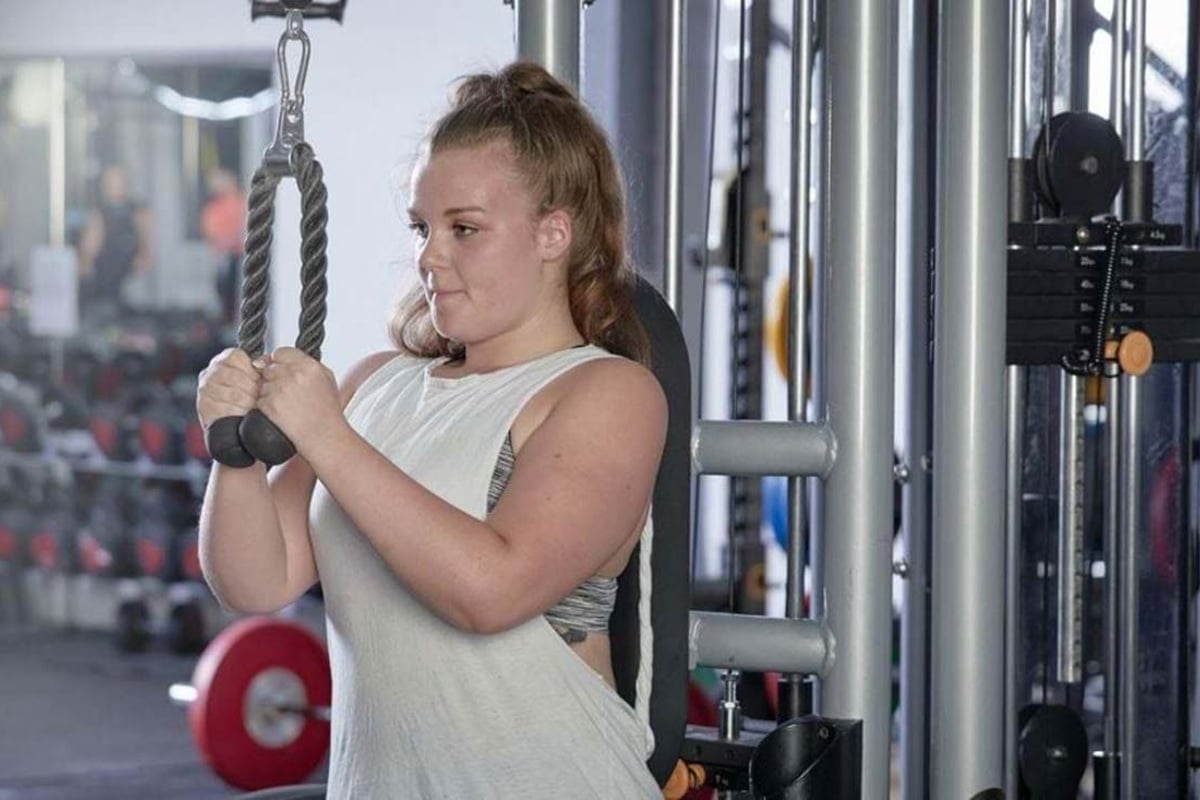 Femme utilisant une machine à câbles pour triceps en salle avec poids en arrière-plan