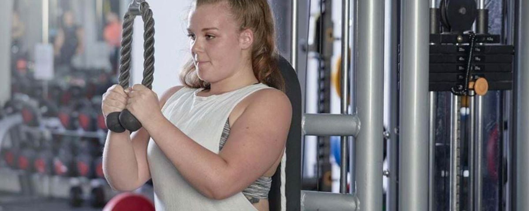 Femme utilisant une machine à câbles pour triceps en salle avec poids en arrière-plan
