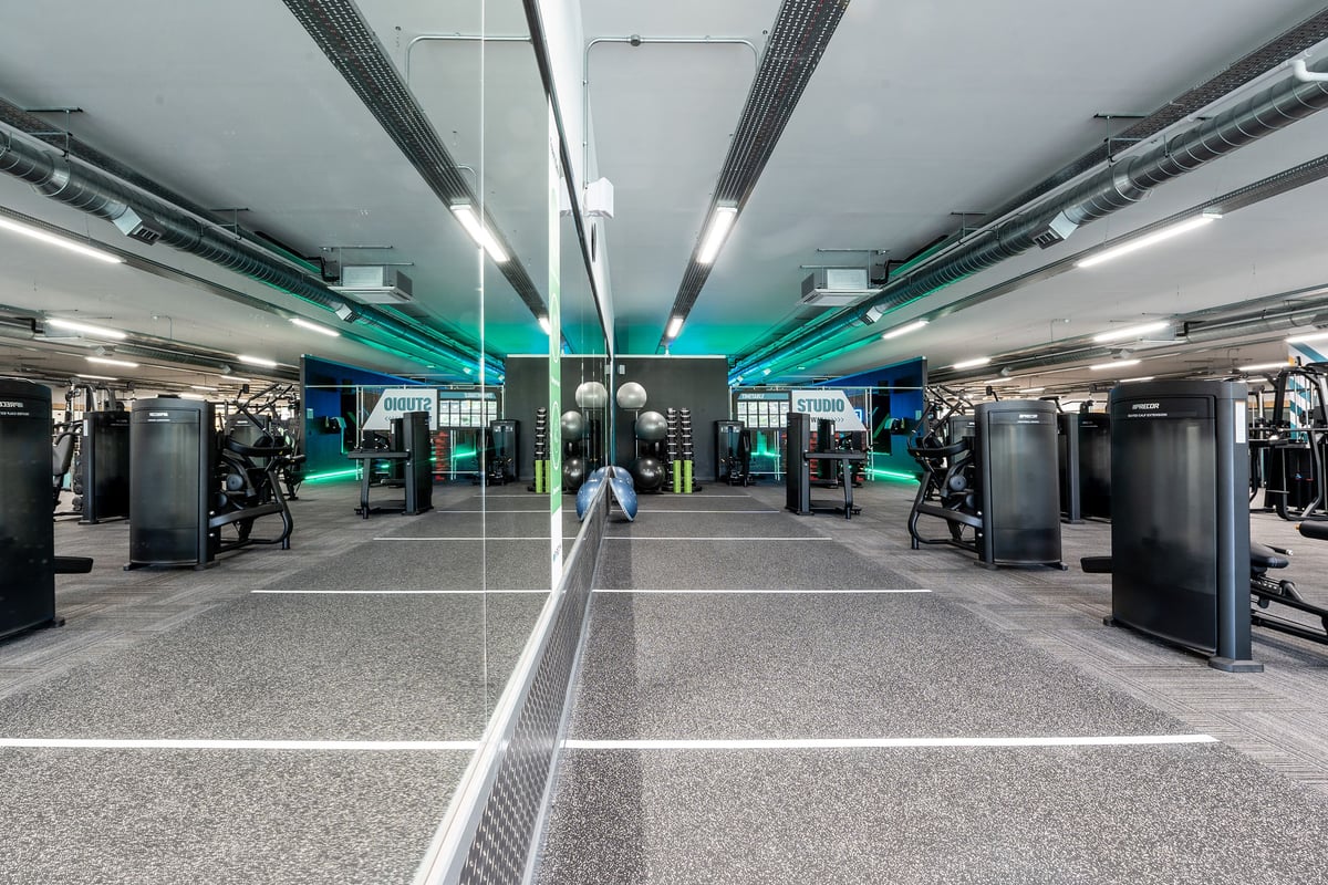 PureGym Witney: Rows of cardio machines, weight stations, and mirrored walls in a vibrant interior gym space.