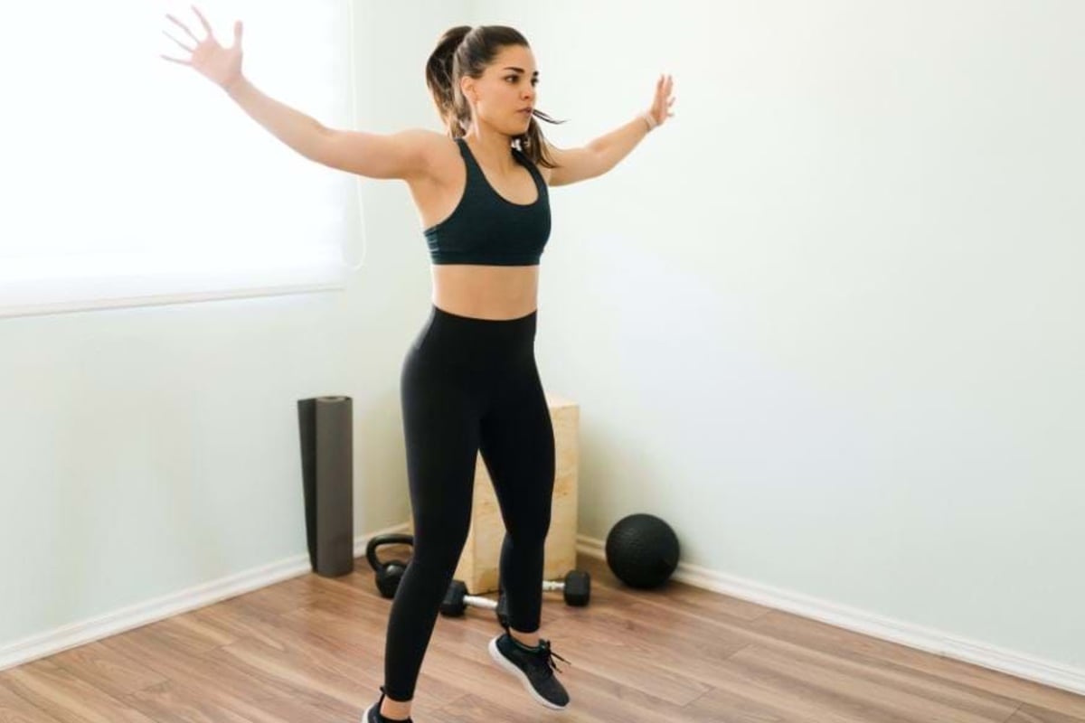 Woman in black sportswear exercising with arms stretched out in a bright room