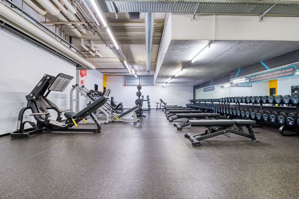 PureGym Dübendorf: PureGym fitness area with rows of weight benches and resistance machines.