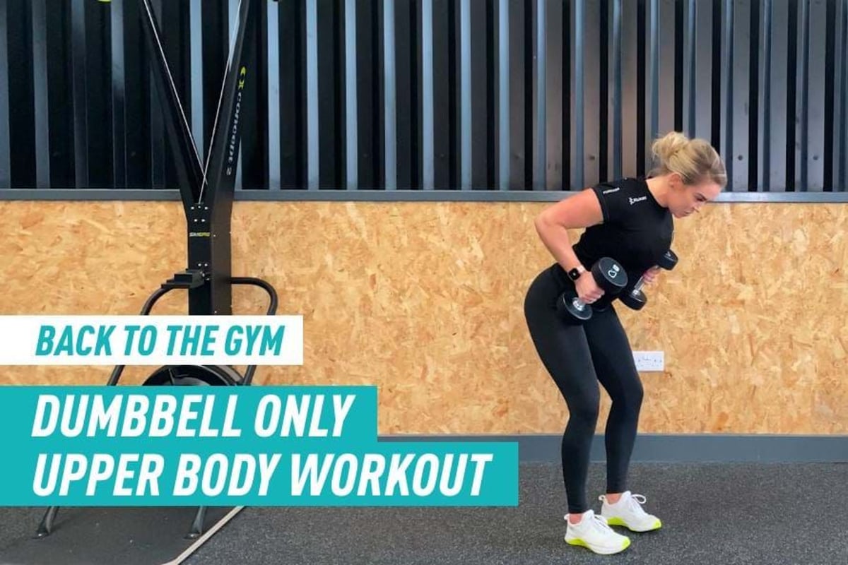 Woman in black workout clothes lifting dumbbells in gym with wooden wall background