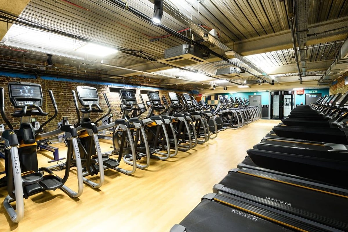 PureGym London Tower Hill: Rows of treadmills and exercise bikes in a dimly lit gym interior with exposed ceiling.
